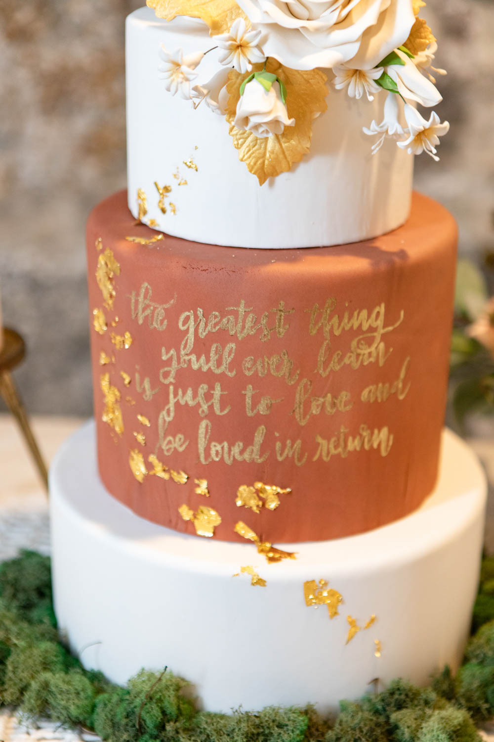 gold script on three-tier wedding cake An all-female vendor team created this gorgeous burgundy and gold LGBTQ+ wedding inspiration at The White Room in Worcester, Massachusetts. The venue is situated in a historic mill building. The models are a real-life couple who are getting married this October. We love the burgundy contrasted with blush, rusty orange and the leather and gold touches.