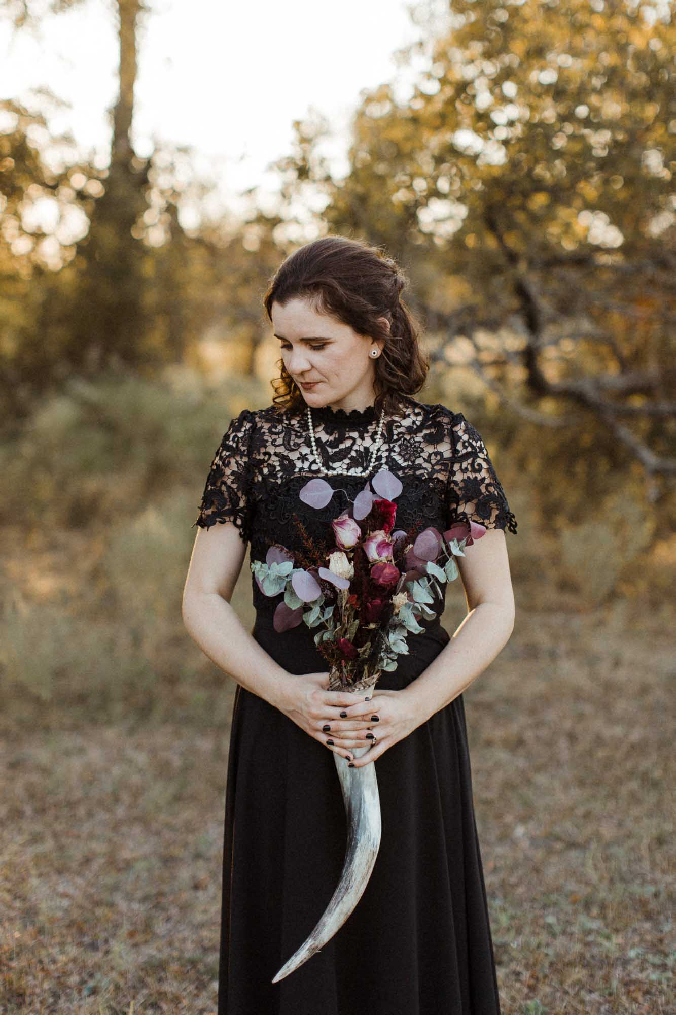 Beautifully gothic Texas wedding with creative details, photo by Leah Thomason Photography, featured on Equally Wed, the LGBTQ+ wedding magazine bride in black wedding gown holding bouquet in animal horn