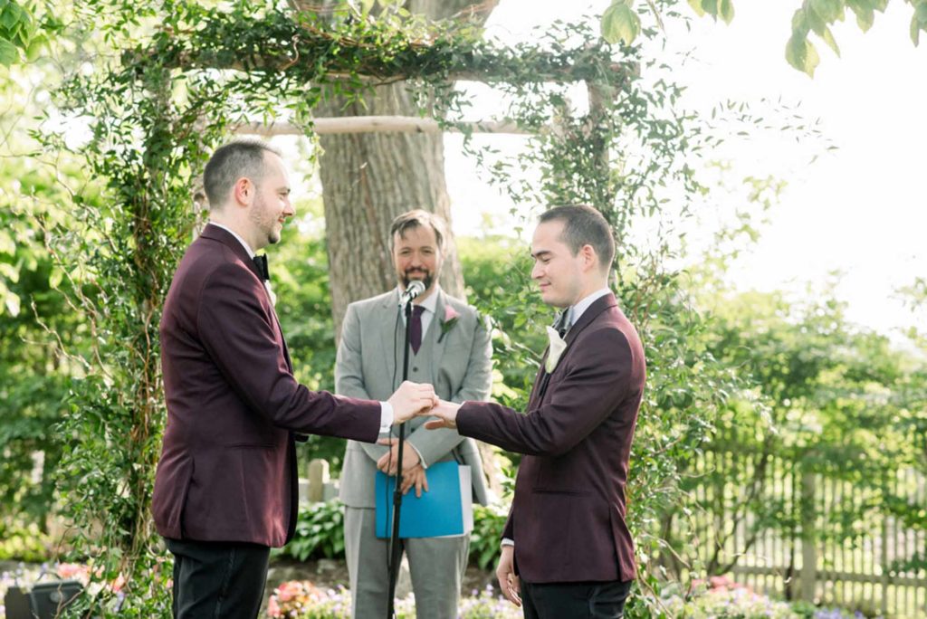 gay grooms exchange wedding rings LGBTQ+ wedding featured on Equally Wed magazine with two grooms Brian + Brett: Hudson Valley garden wedding with shades of purple Upasana Mainali Photography outdoor wedding ceremony