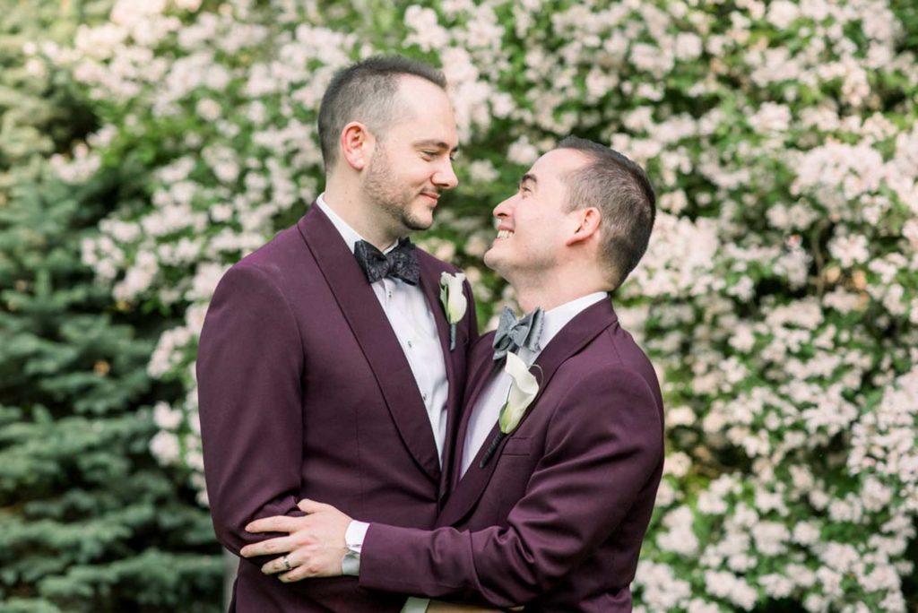 men in love grooms in purple jackets holding hands LGBTQ+ wedding featured on Equally Wed magazine with two grooms Brian + Brett: Hudson Valley garden wedding with shades of purple Upasana Mainali Photography outdoor wedding ceremony