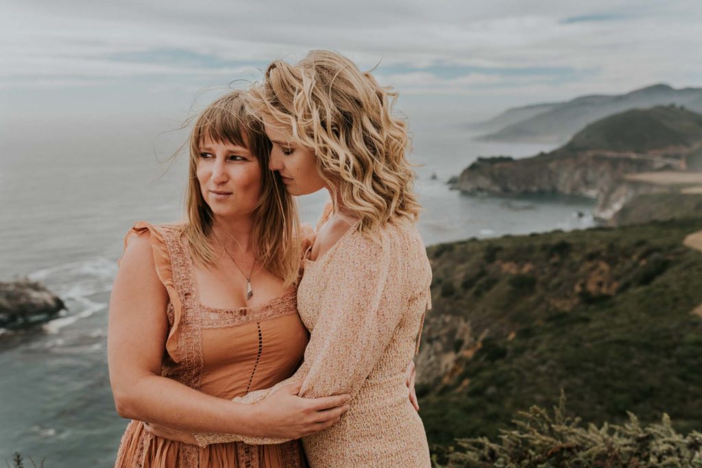 Magical engagement photo session in Big Sur. Photography by Heather K. Purdy. Featured on Equally Wed, the leading LGBTQ+ wedding magazine and wedding vendor directory of LGBTQ+ inclusive wedding pros. pictured: Two women in love wearing boho dresses kissing on the coast of California with the ocean in the background