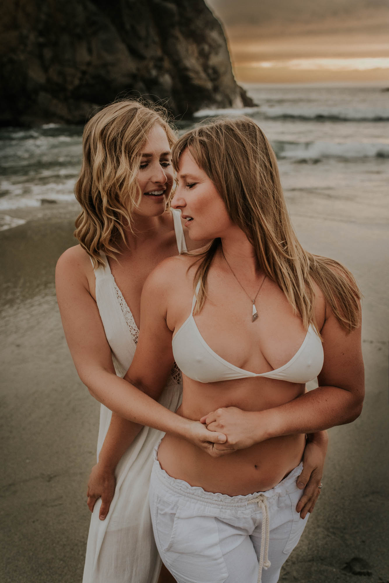 Magical engagement photo session in Big Sur. Photography by Heather K. Purdy. Featured on Equally Wed, the leading LGBTQ+ wedding magazine and wedding vendor directory of LGBTQ+ inclusive wedding pros. romantic sexy image includes two blonde women in love in white outfits on beach