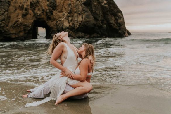 Magical engagement photo session in Big Sur. Photography by Heather K. Purdy. Featured on Equally Wed, the leading LGBTQ+ wedding magazine and wedding vendor directory of LGBTQ+ inclusive wedding pros. romantic sexy image includes two blonde women laughing in love in white outfits on beach