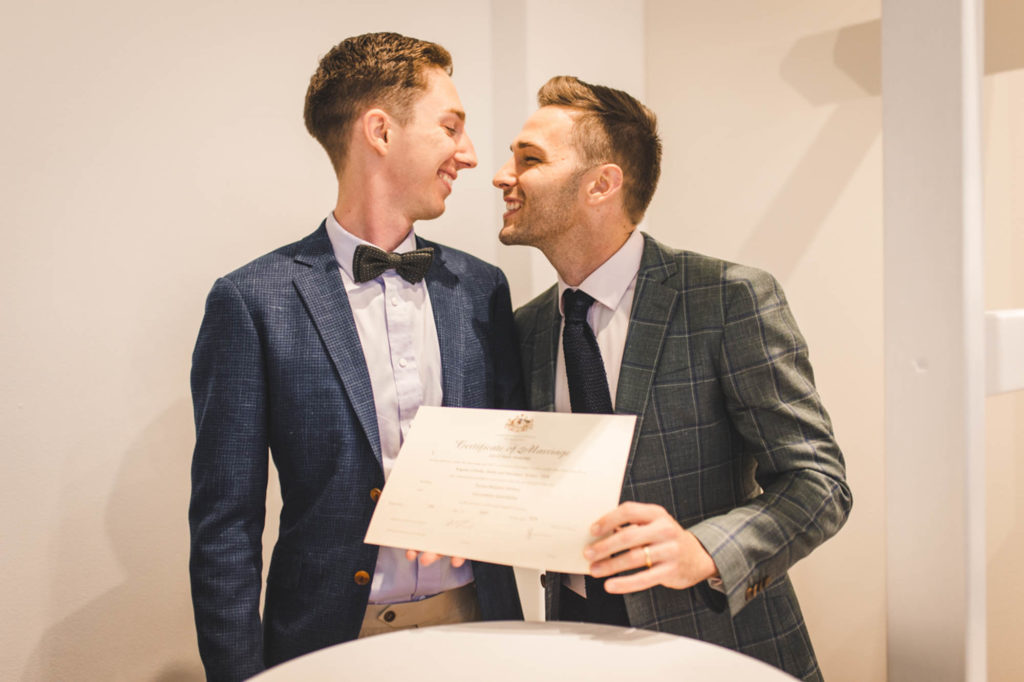 After a four-month engagement, Joel and Thomas married in a Sydney, Australia, microwedding. Photo by Chris Gray Photomedia. Published on Equally Wed, the world's leading LGBTQ+ wedding magazine and wedding directory of LGBTQ+ inclusive wedding vendors and venues. pictured: two grooms holding their marriage certificate
