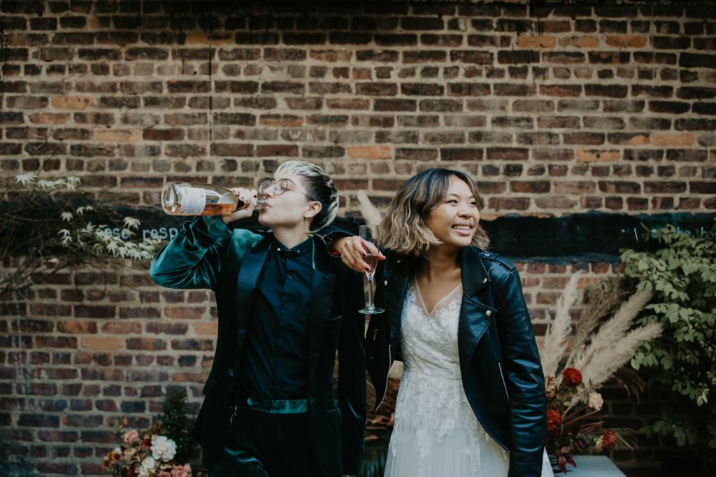 Outdoor Brooklyn microwedding styled shoot | Photography by Lucie B Photography | Featured on Equally Wed, the world's leading LGBTQ+ wedding magazine | drinking rose out of the bottle, velvet jacket, leather jacket, LGBTQ+ couple