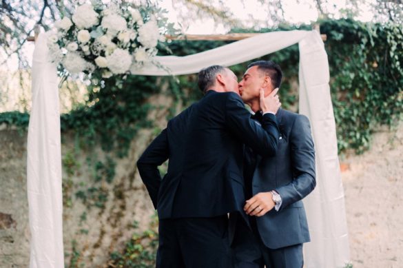 Two men kiss under their wedding arch.