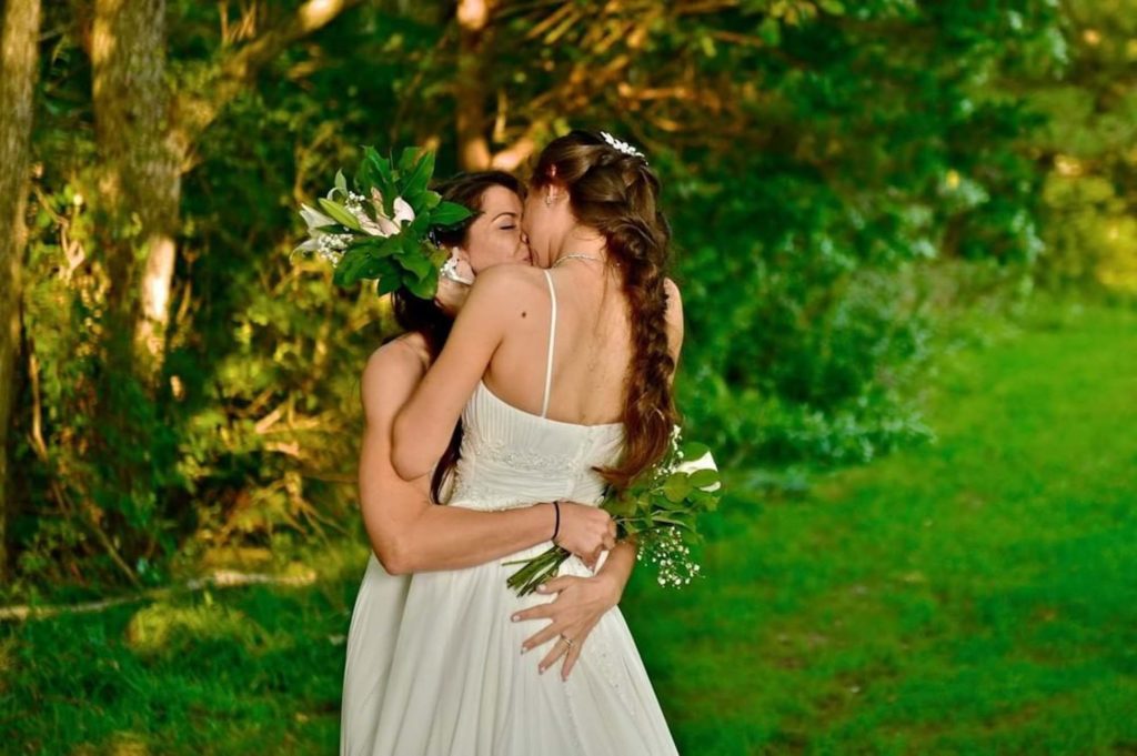 These lesbian brides accidentally wore the same dress. The first look photos are priceless | Sarah Smith Studios | Featured on Equally Wed, the leading LGBTQ+ wedding magazine - mountain, sunset, white dress, green suit