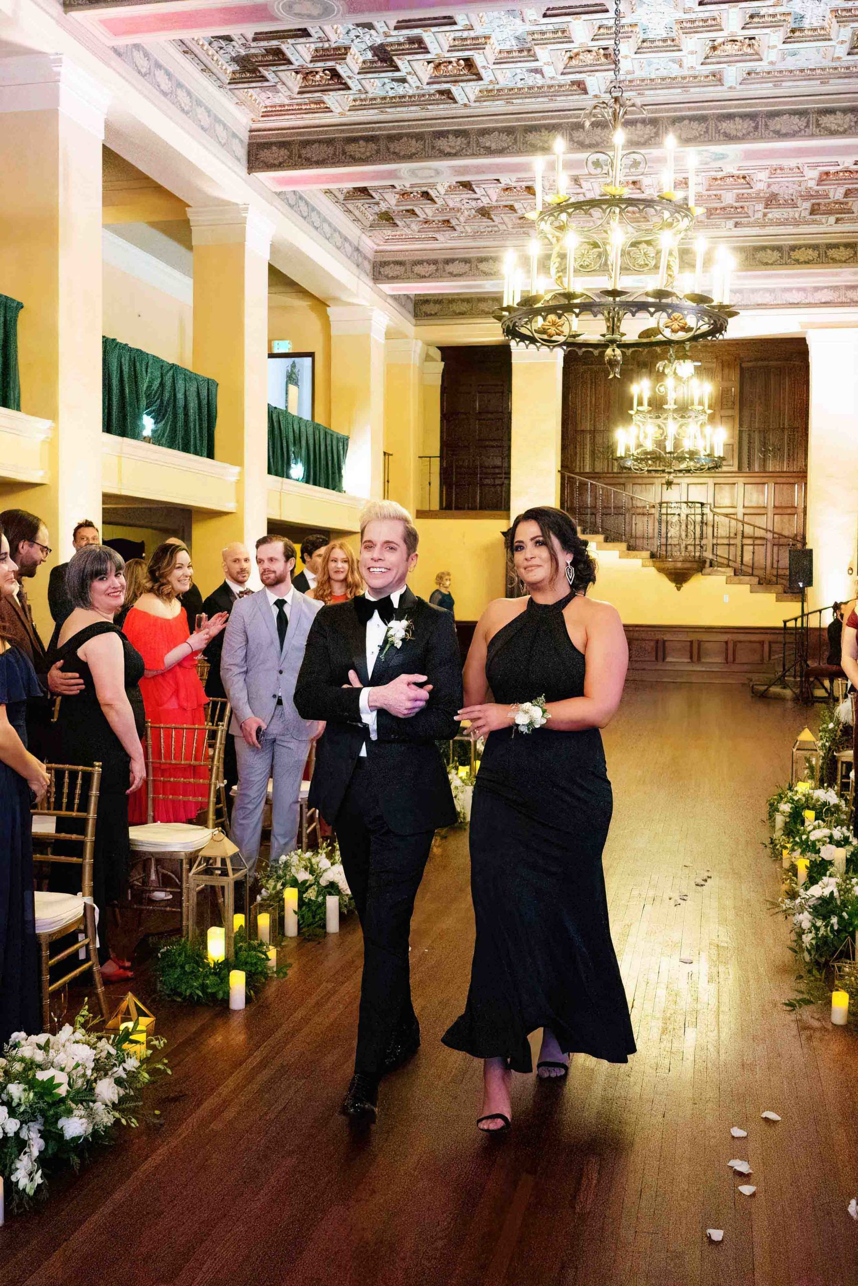 groom escorted up aisle with a woman in a dark dress while wedding guests watch