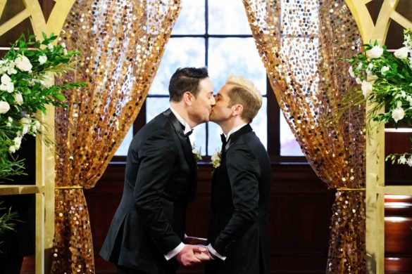 gay men kiss under wedding arch with gold sparkle drapes