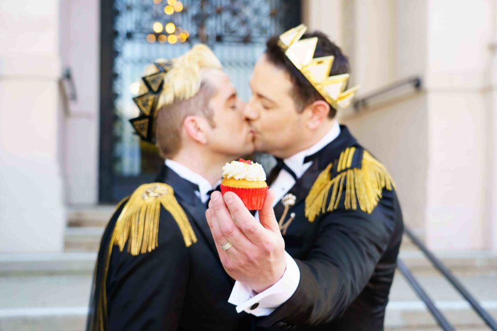 two men kissing holding a cupcake and wearing black and gold crowns for Hollywood gay wedding