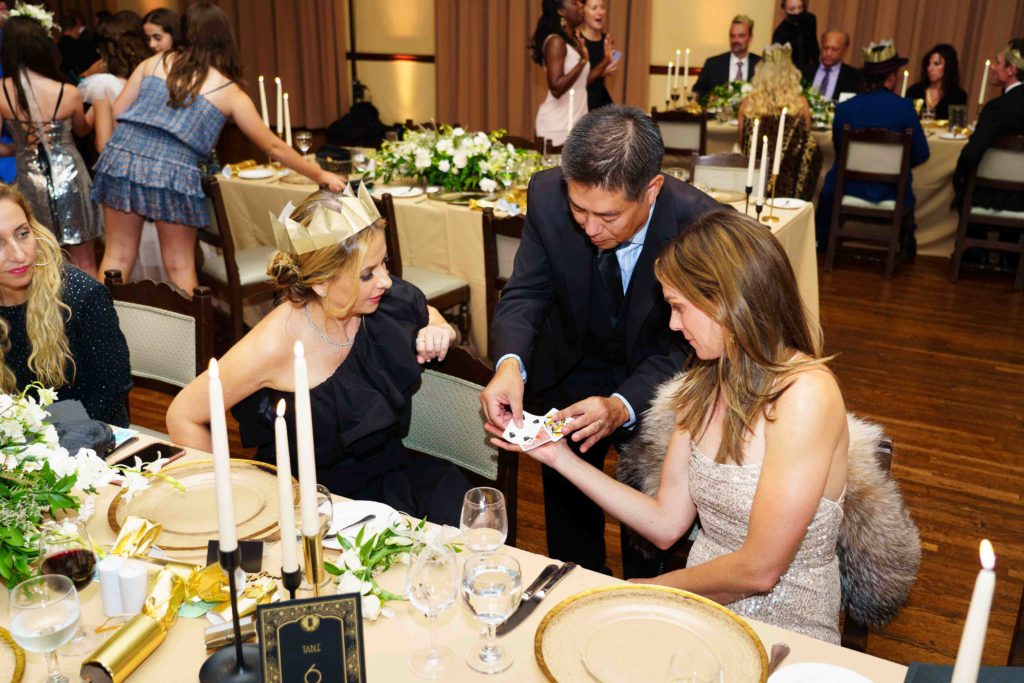 Sarah Michelle Gellar and friend look on while a magician does card tricks at wedding
