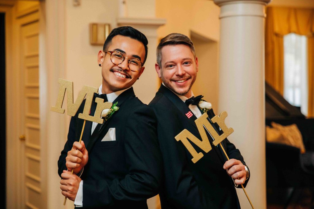 gay grooms smile and hold Mr and Mr signs