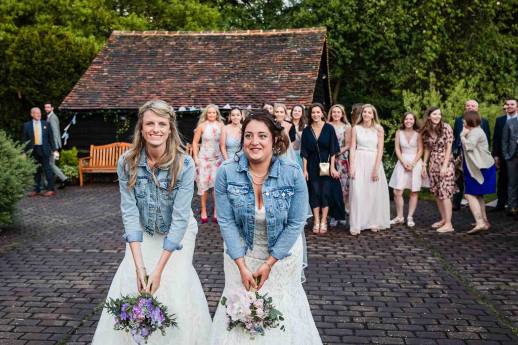 brides in jean jackets do a bouquet toss at a lesbian wedding