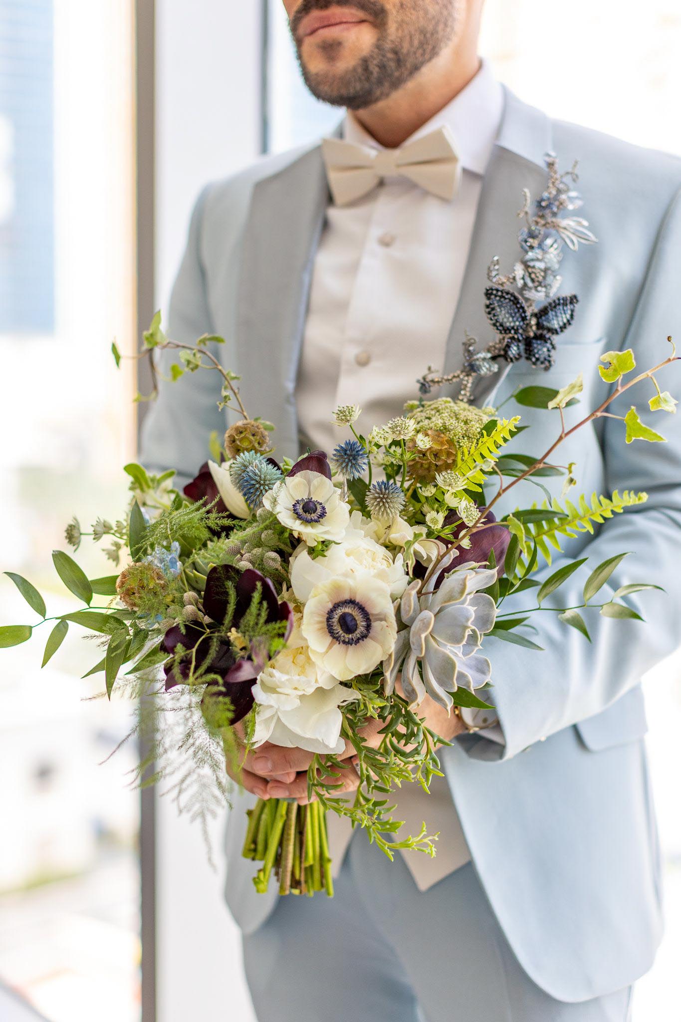 groom in blue suit holding his bouquet