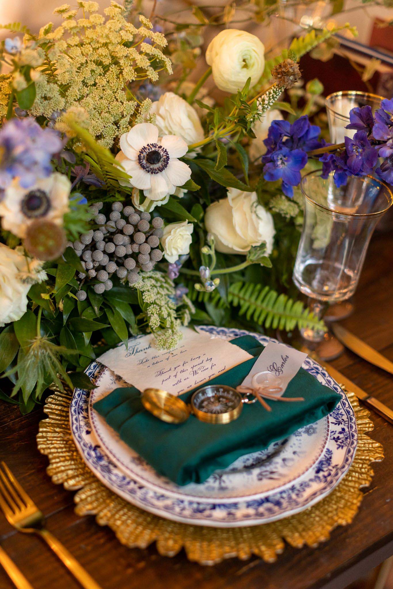 wedding reception table setting with compass, anemones, green and gold accents