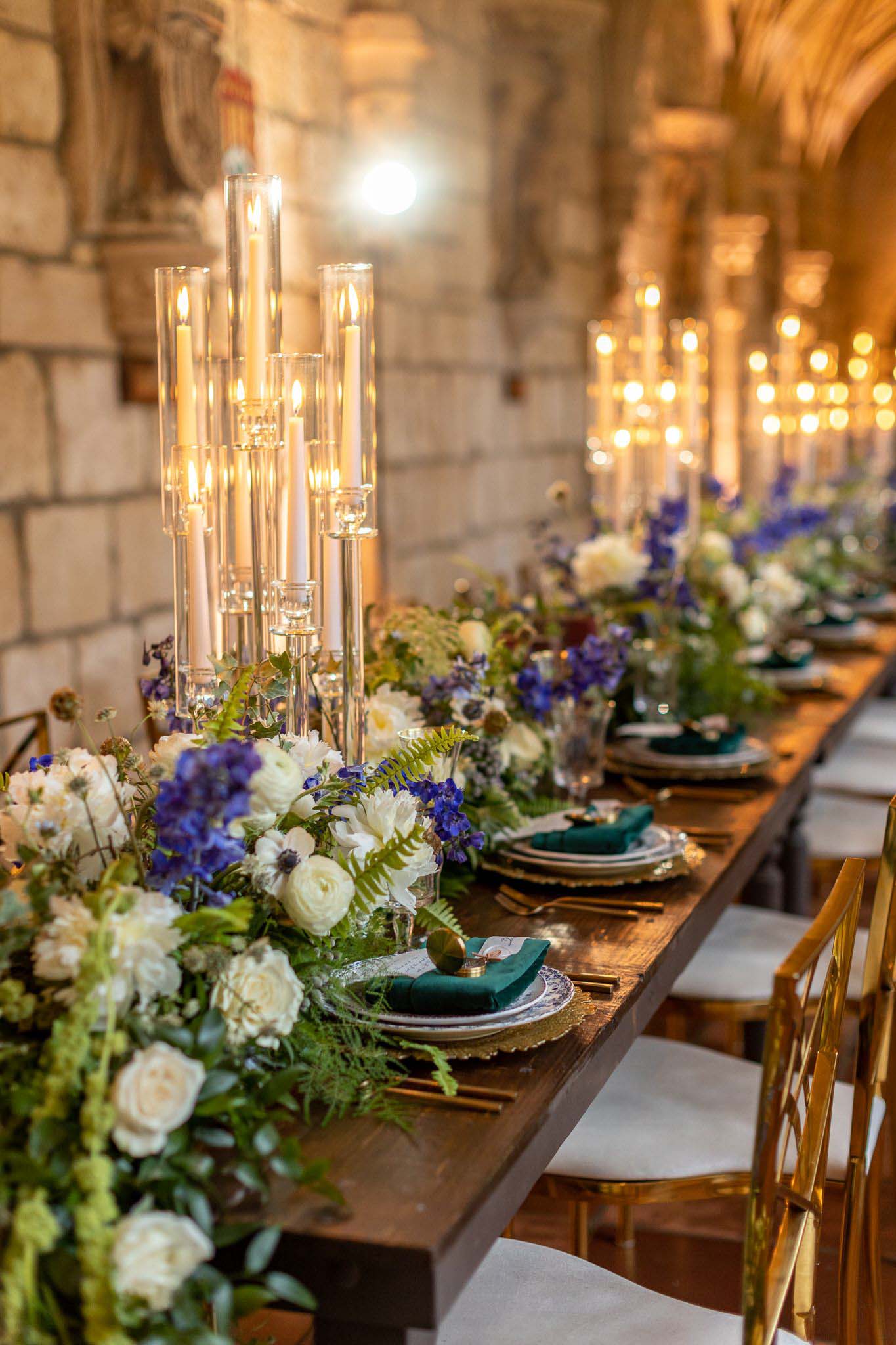 стол для свадебного приема с высокими светильниками, белыми и фиолетовыми цветами, зелеными салфетками и зеленью