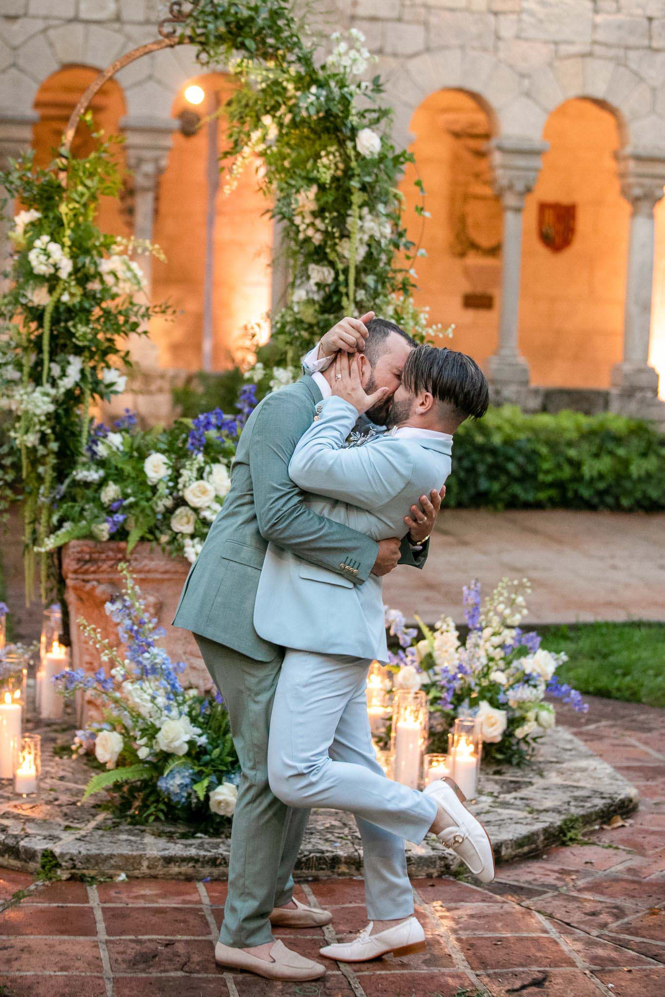 gay grooms kiss after saying I do surrounded by a garden of flowers