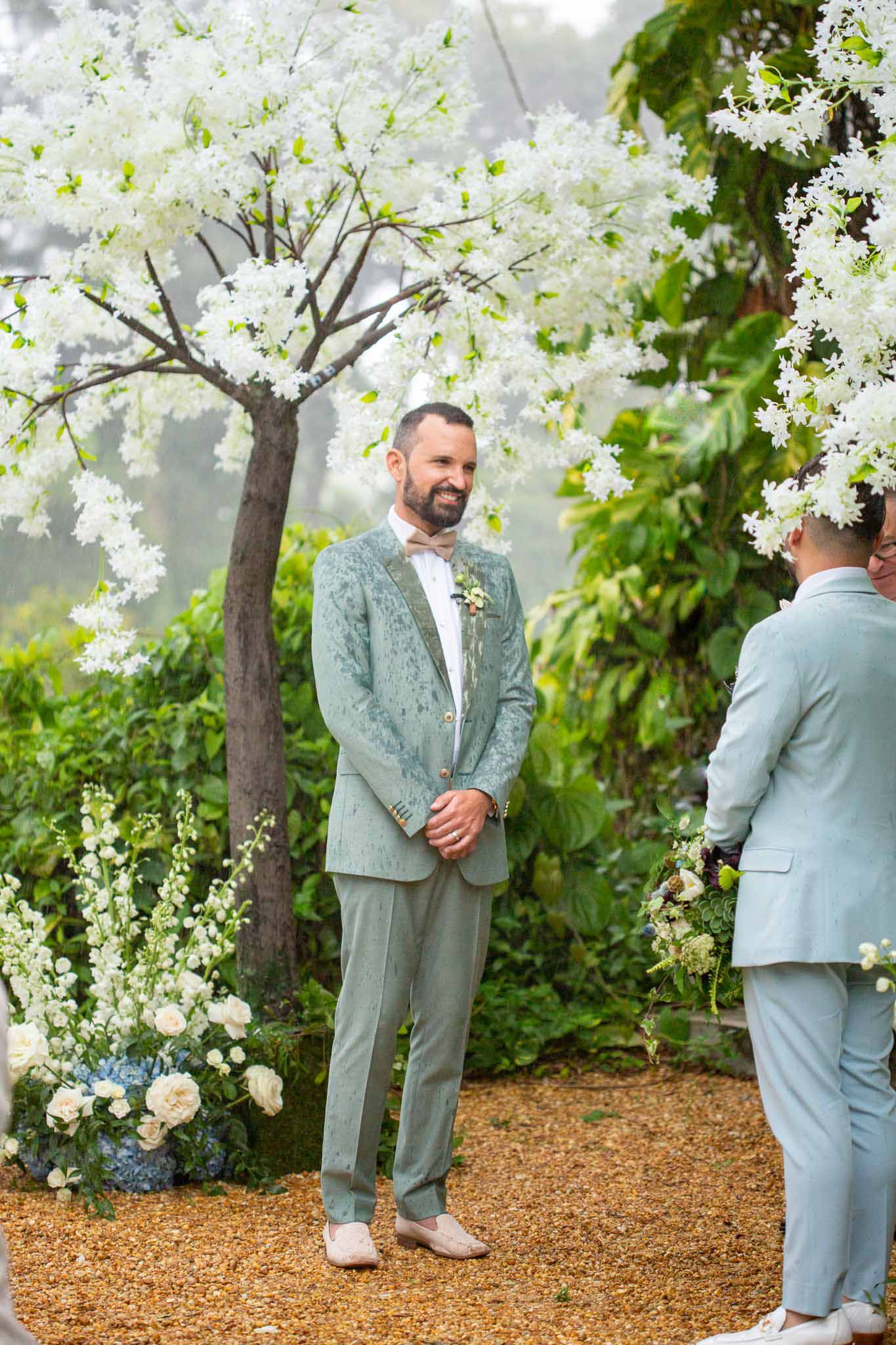 two grooms at their outdoor wedding altar surrounded by white flowers