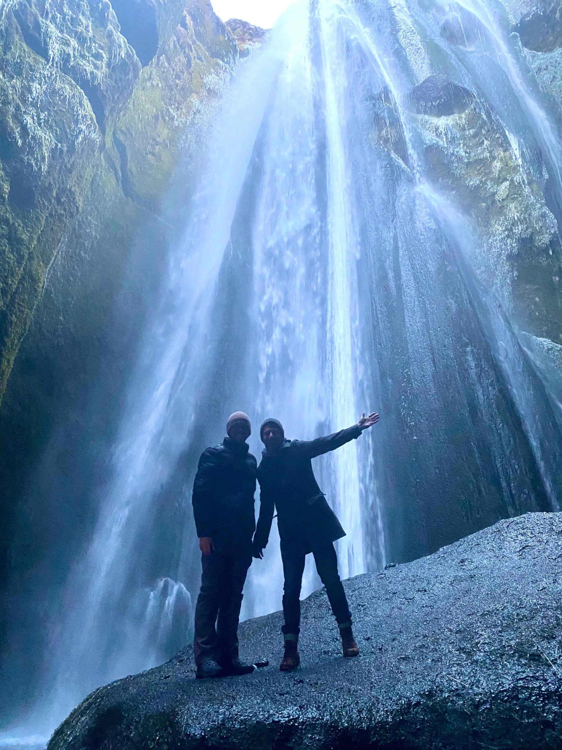 gay couple stand in front of waterfalls LGBTQ+ honeymoon Iceland