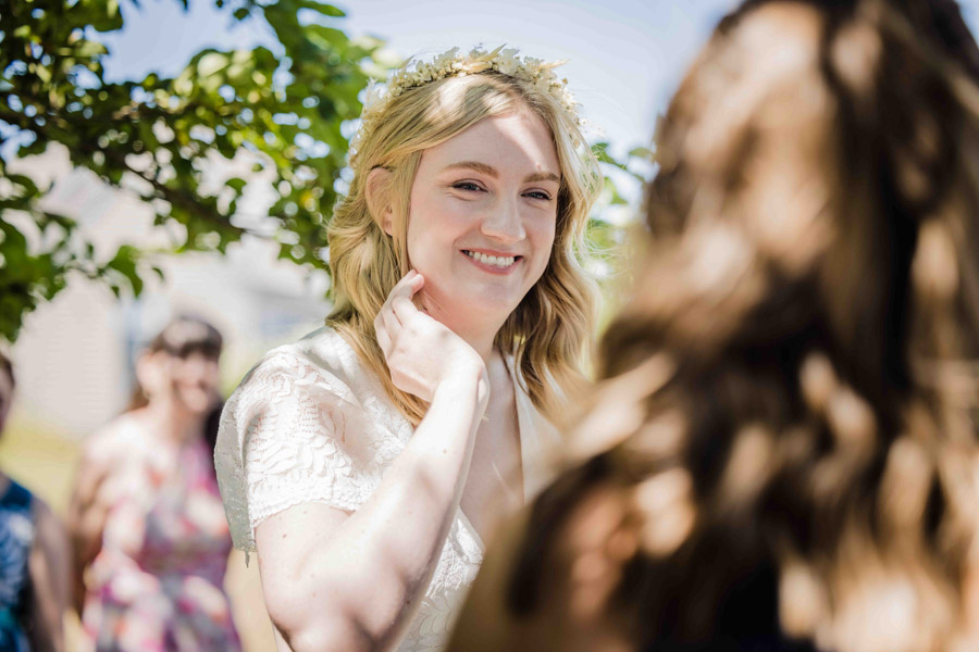 blonde marrier wearing a white flower crown smiles during wedding ceremony