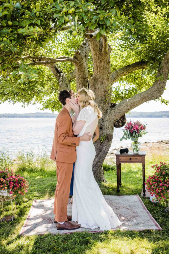 LGBTQ+ couple kisses after getting married under an apple tree at their outdoor summer wedding