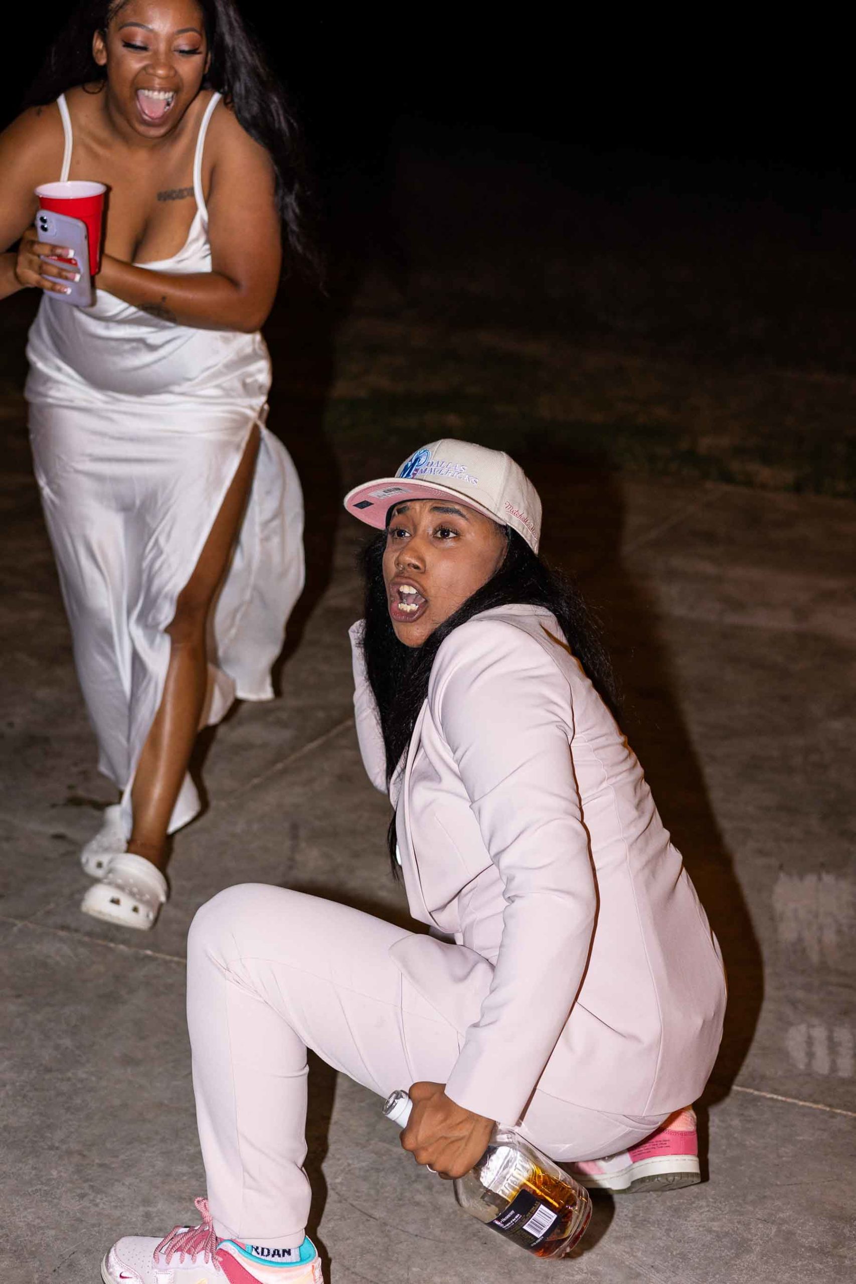 Black lesbian couple dancing, one is in a hat and a pink suit and the other is wearing a silk white dress with thin straps