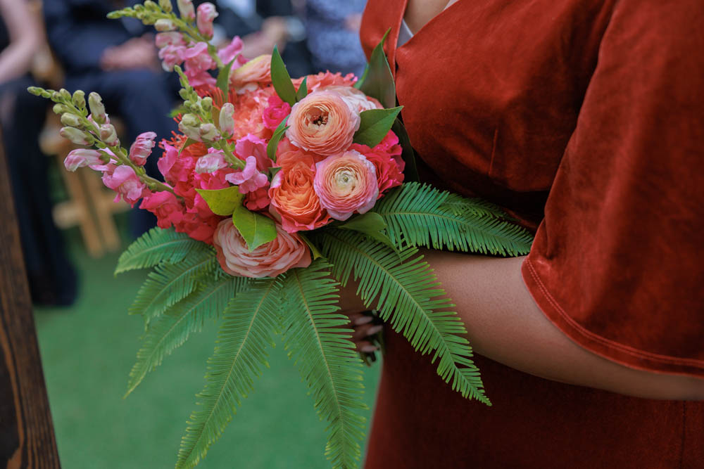 wedding bouquet with shades of pink held by a person wearing a dark orange wedding attendant dress