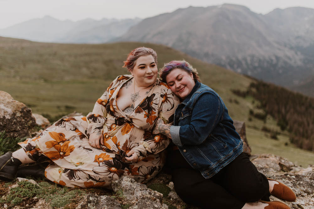 two white women holding each other while sitting outdoors on a mountain top. 