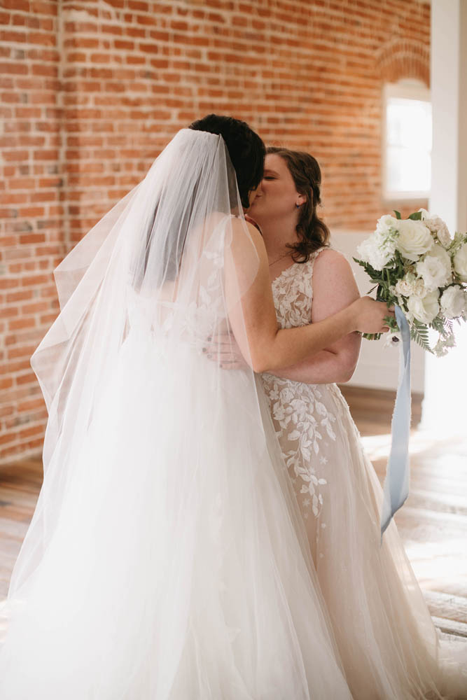 two brides kiss. they're wearing white wedding gowns.