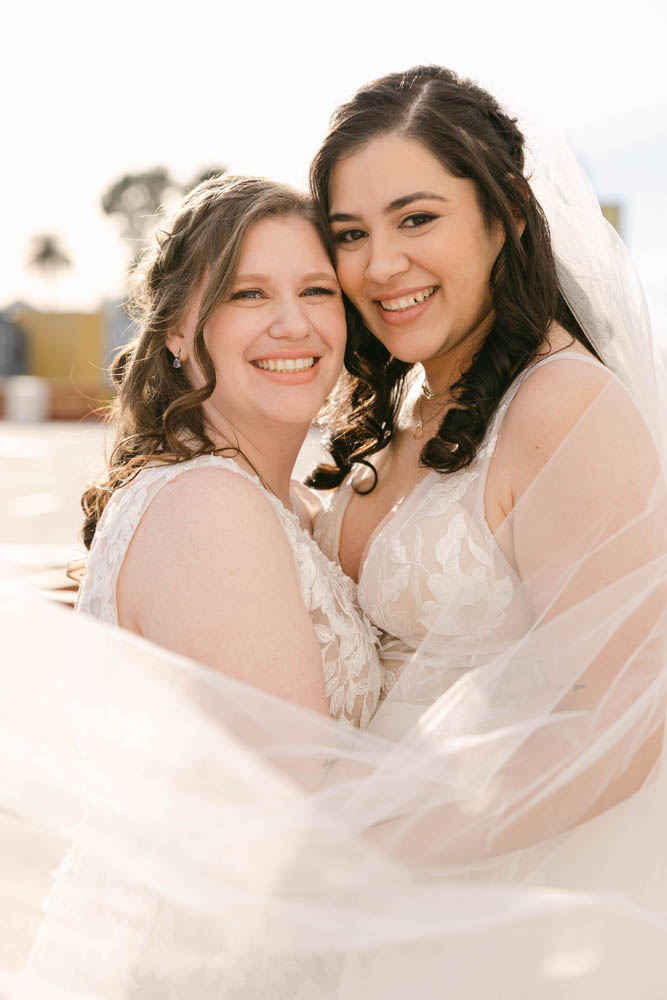 two women hold each other while smiling and look at the camera. they're very happy because it's their wedding day!
