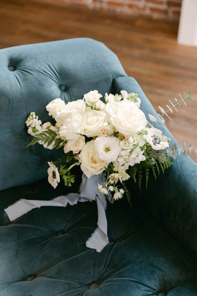 wedding bouquet of white flowers and dusty blue ribbon on a blue sofa