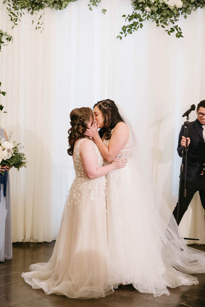 two brides in long wedding gowns kiss after marrying