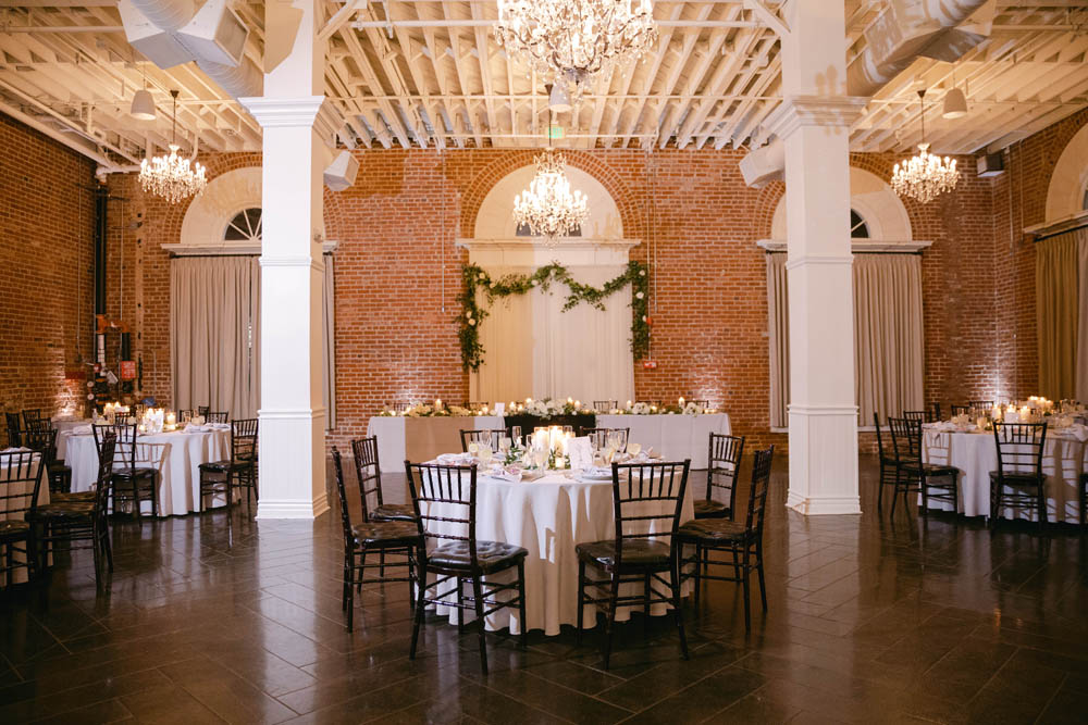 wedding reception with brick walls, brown floors, black chairs, white linens, green garland and white flowers