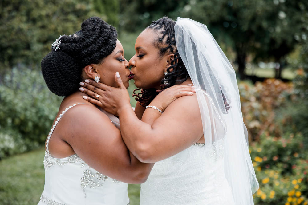 two Black brides kiss in garden