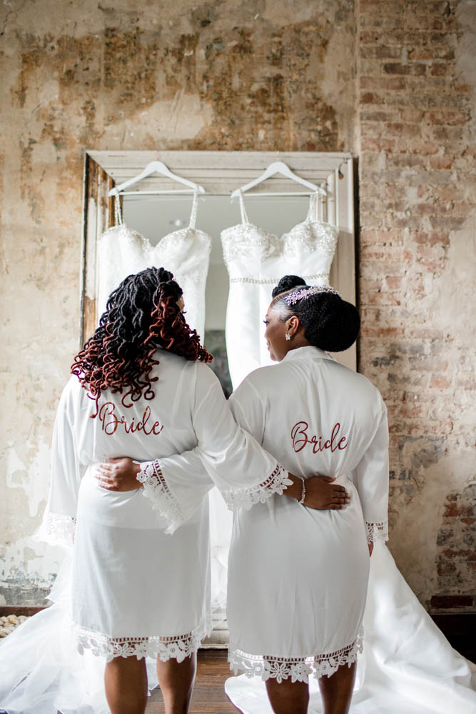 two Black brides in white robes with the word Bride written on the back in pink