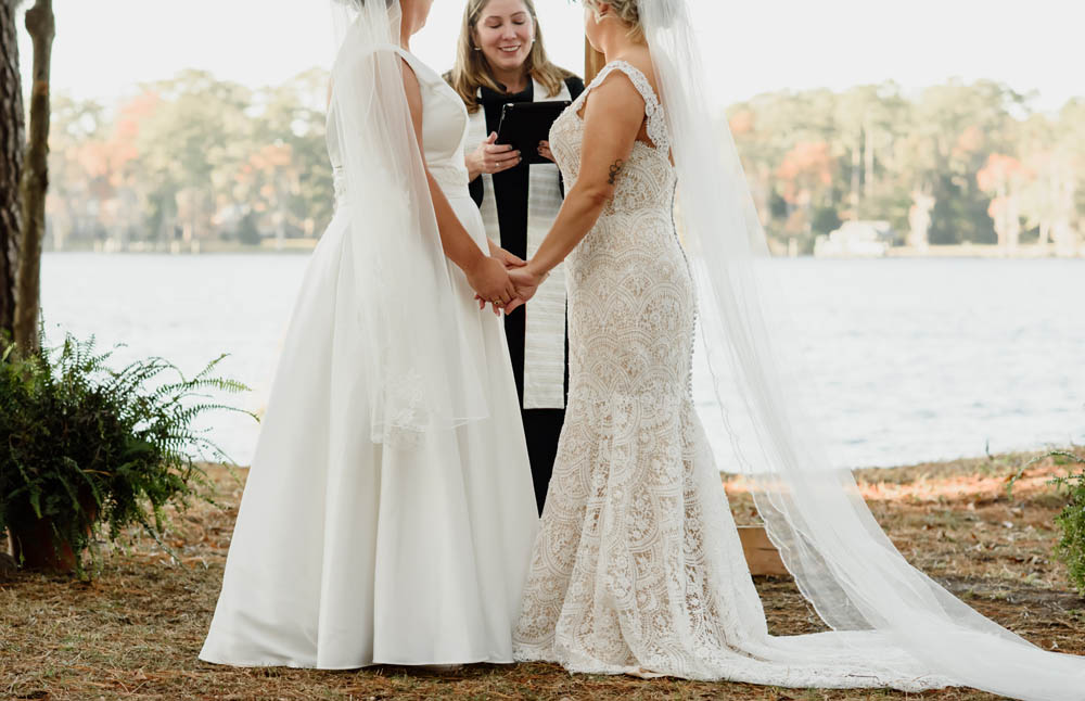 lesbian brides hold hands during their ceremony while their pastor speaks