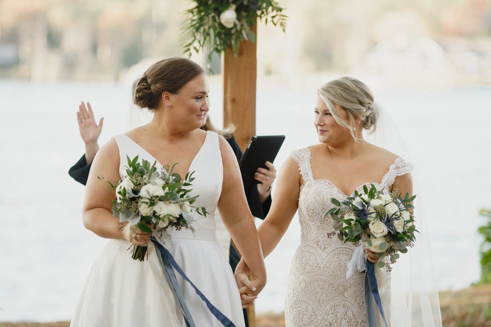 two white lesbian Christian brides with romantic updo hairstyles gaze into each others eyes just after saying "I do"