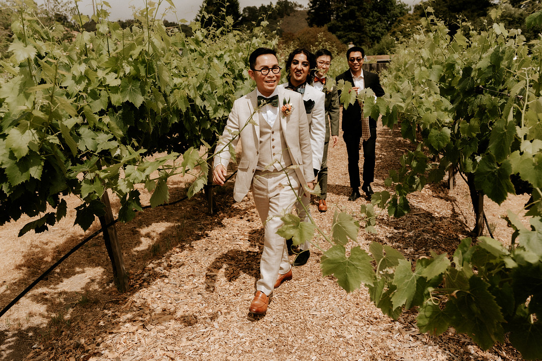 Grooms and their officiant walk through vineyard to their wedding.