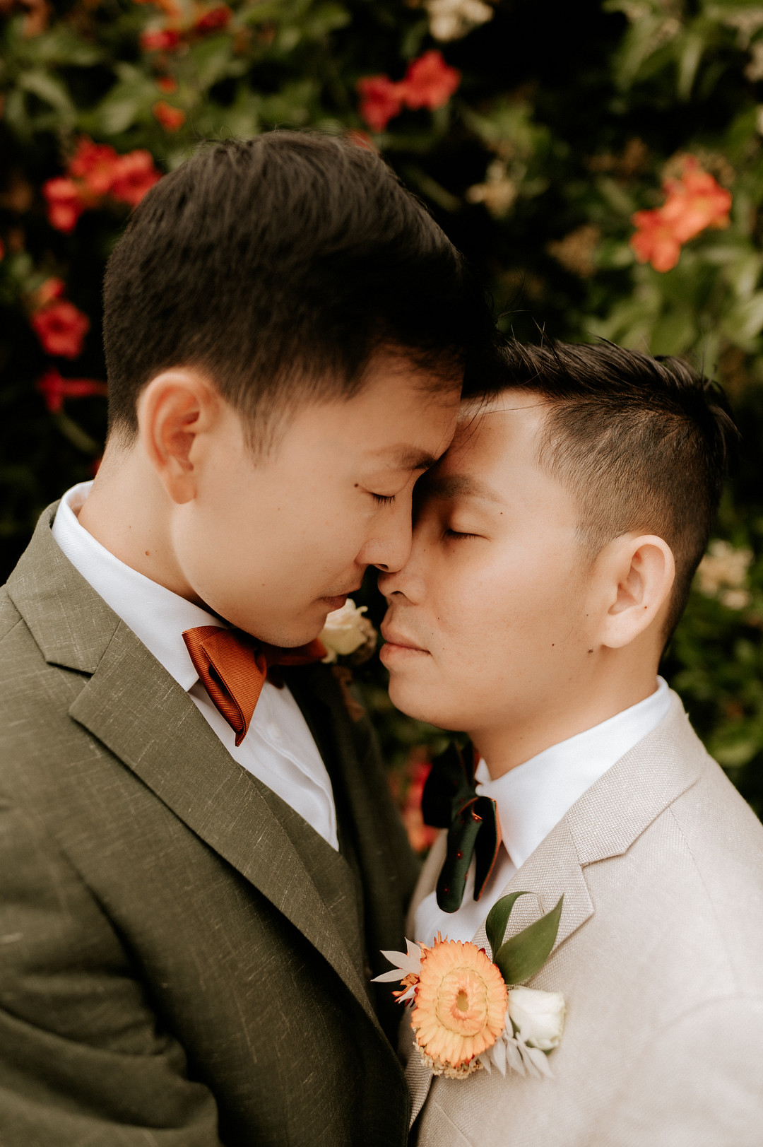 Gay Asian grooms rest their faces together in an intimate moment.