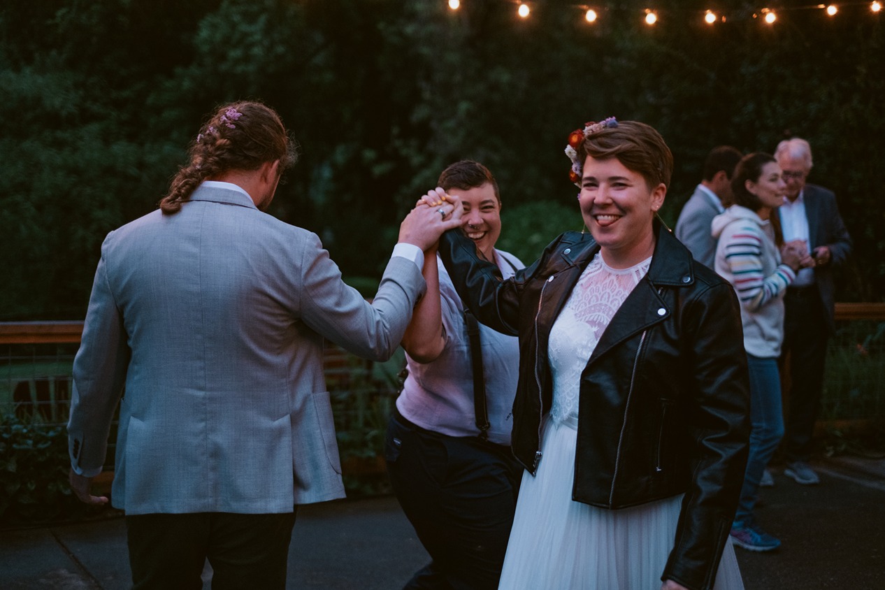 a triad of white people (one man, two women) dances at their throuple wedding
