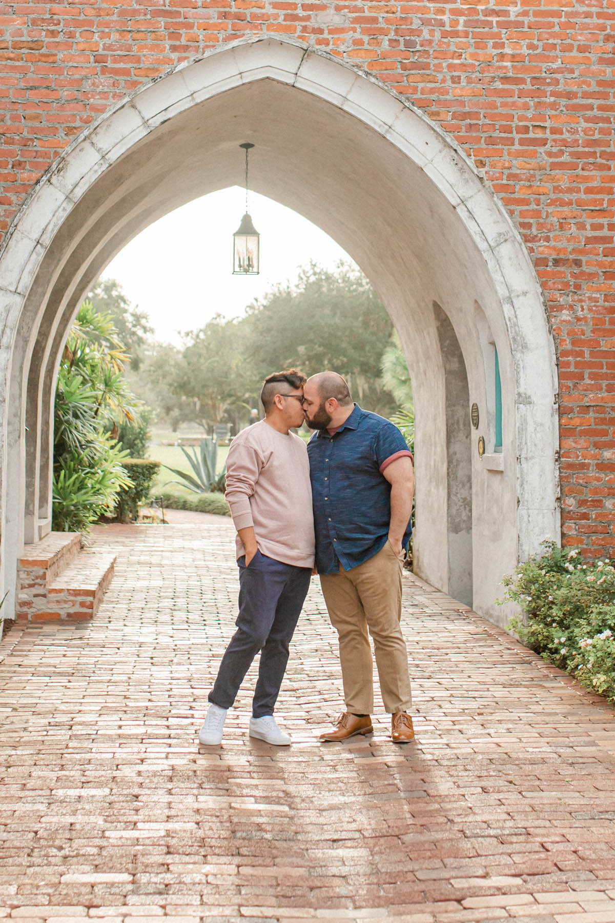 Engaged couple Tony and Daniel stand under a beautiful brick arch, kissing. 