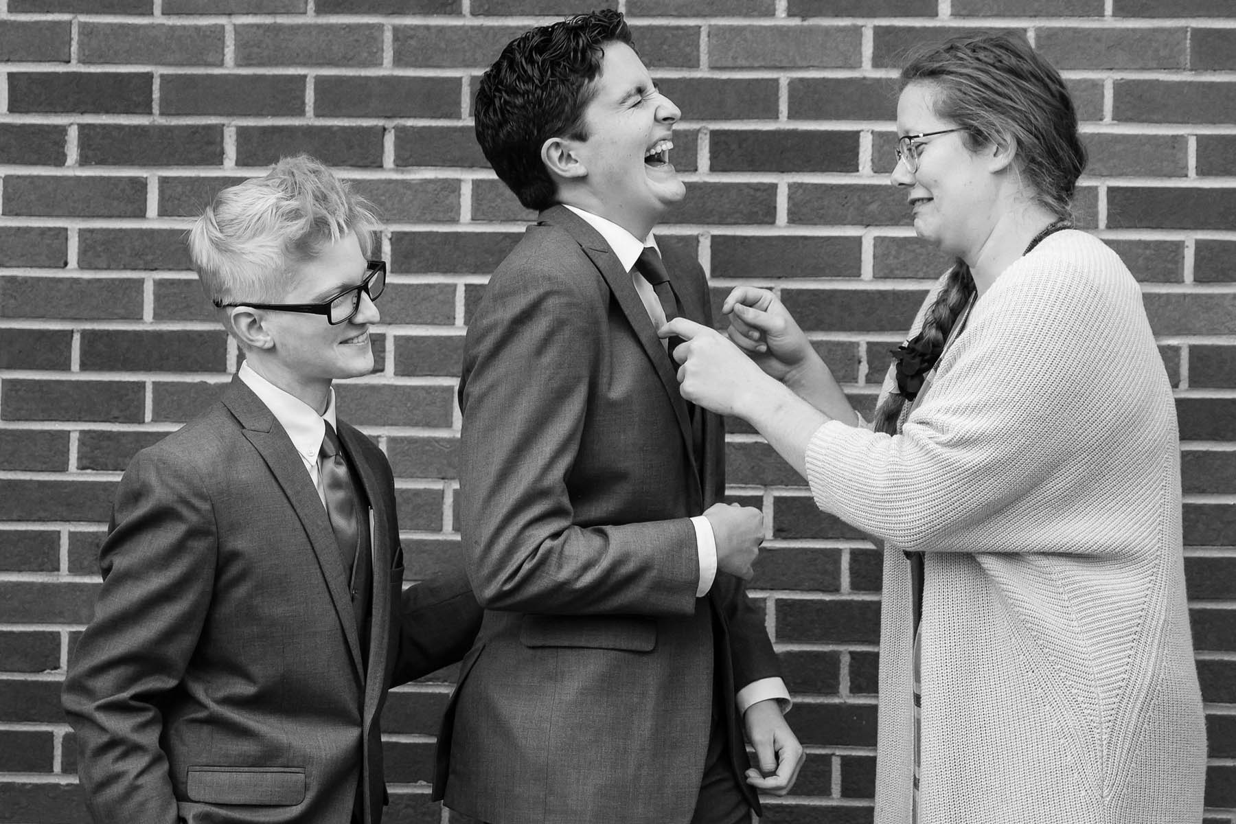 A black-and-white photo of the marriers, with a person in a cardian fixing one fo their ties.