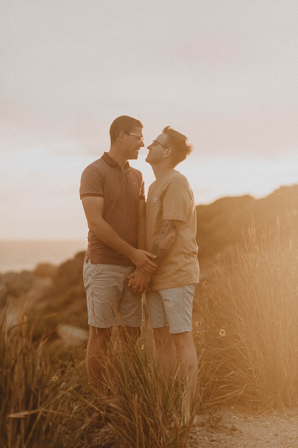 Two men stand, gazing at each other, against a backdrop of golden hour sun.
