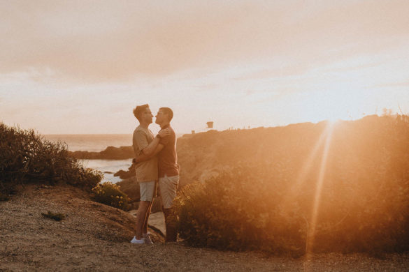 Two white men stand, facing each other, with a Malibu sunset over the Pacific Ocean in the background.