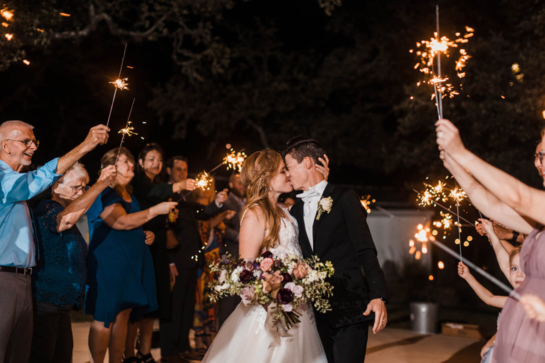 The newlyweds pause for a kiss as they walk down an aisle of their attendants, all holding lit sparklers.