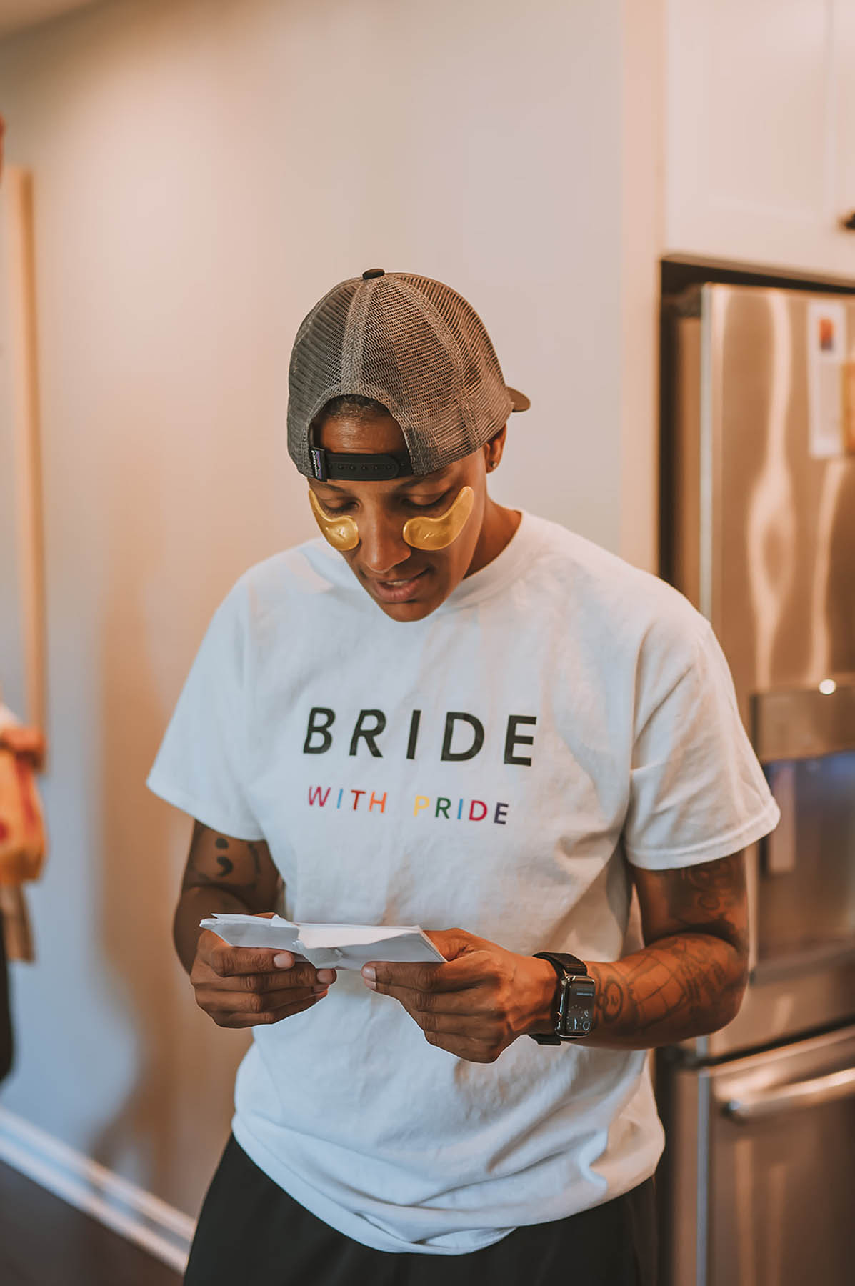 One of the marriers wears a backwards baseball cap and a t-shirt reading "Bride with pride" as she reads a letter from her spouse-to-be.