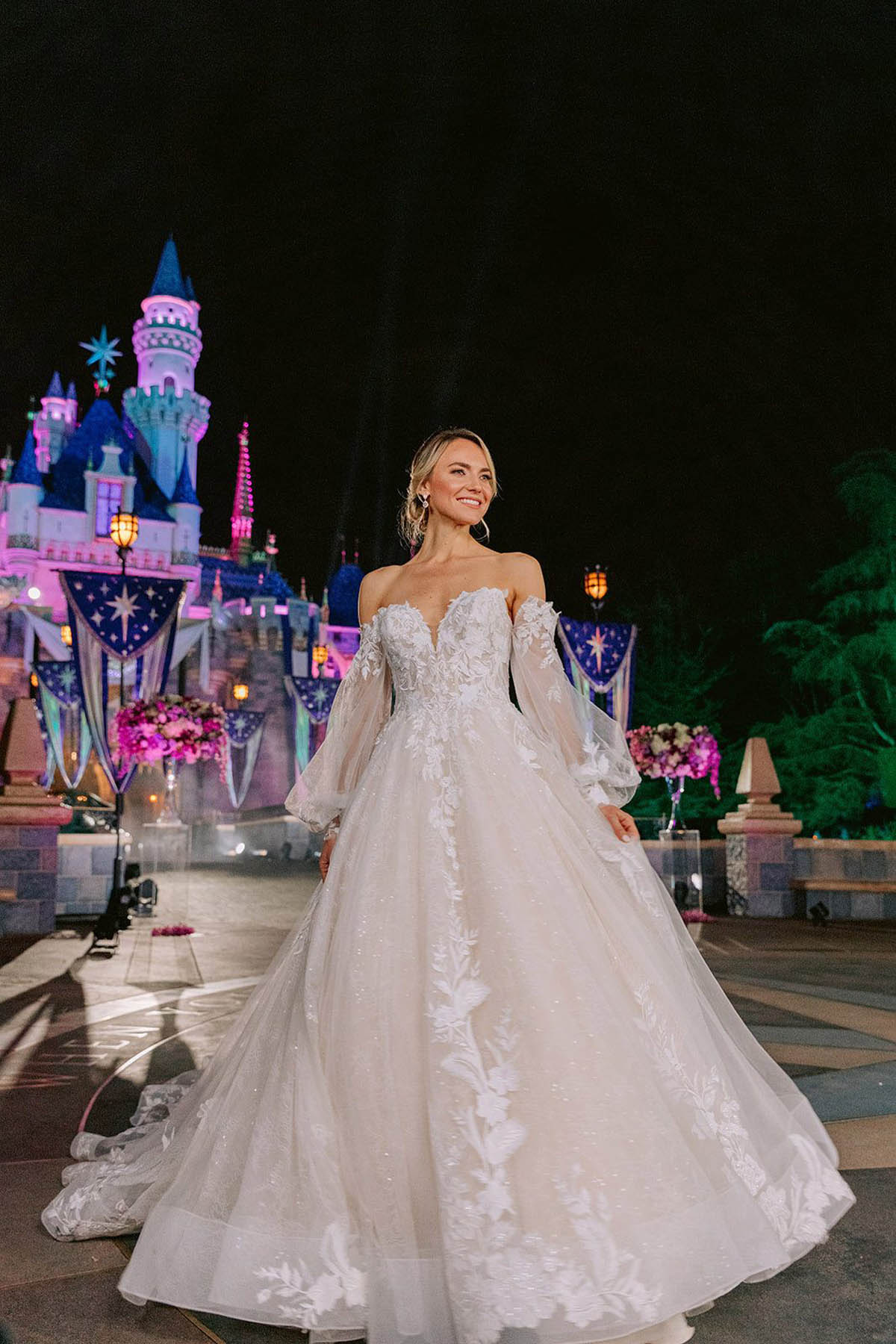A blonde person models a princess-inspired off-the-shoulder white gown.