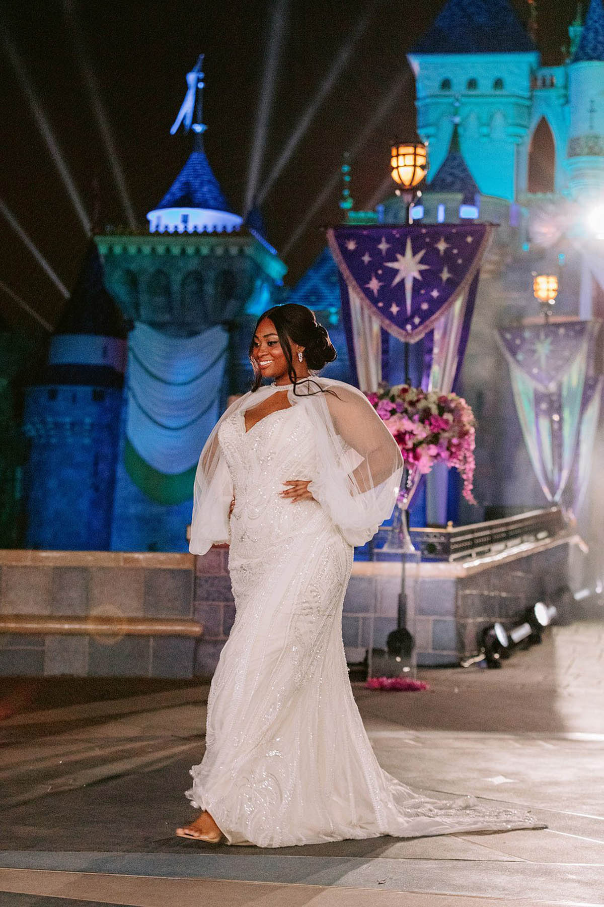 A person of color models a long white gown with pouffy sleeves.