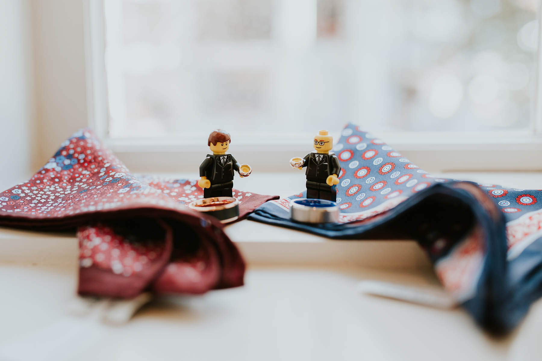 Two Lego figurines that look like the grooms, sitting on burgundy and navy pocket squares.
