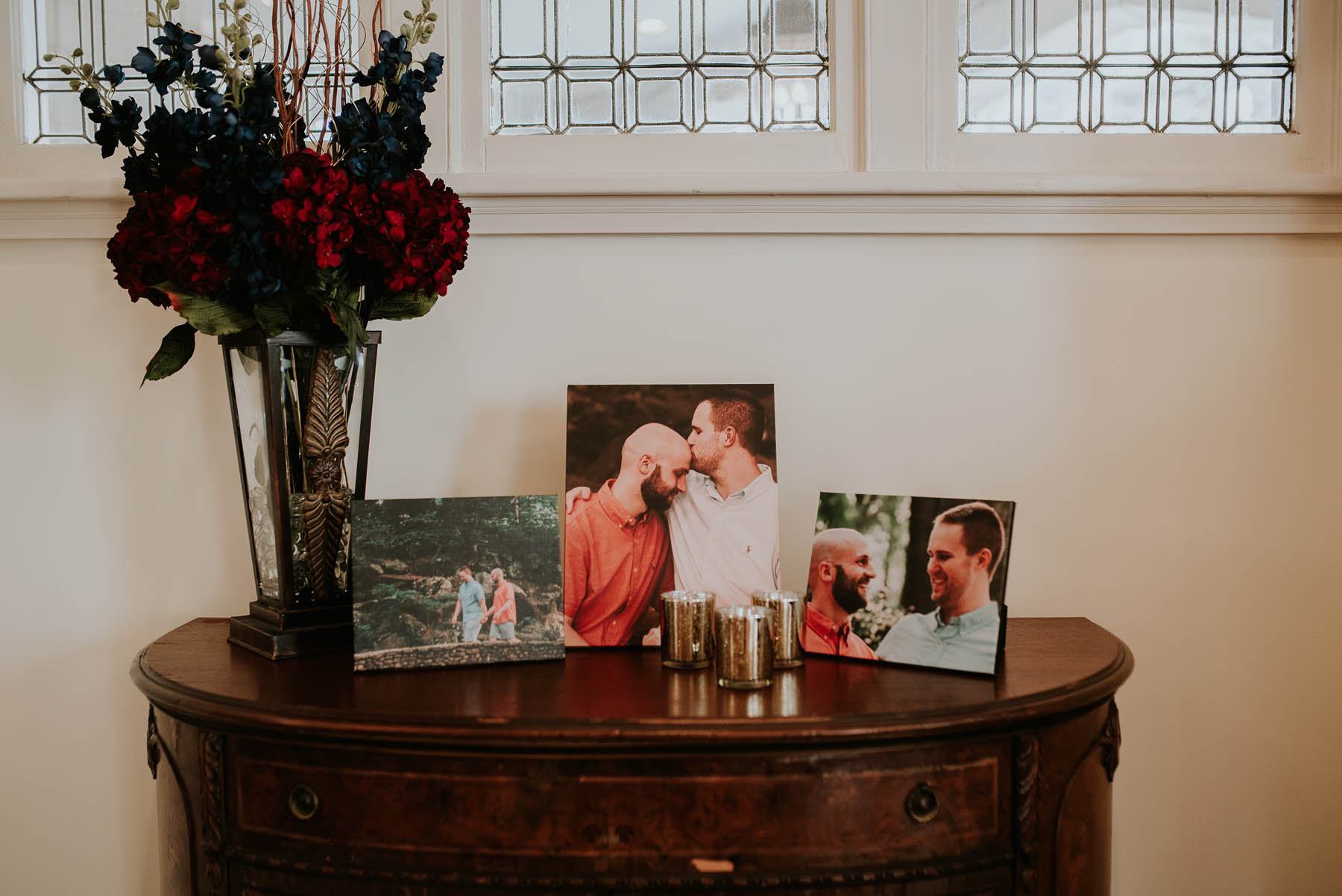 A bistro table with engagement photos on it and navy and burgundy flowers.